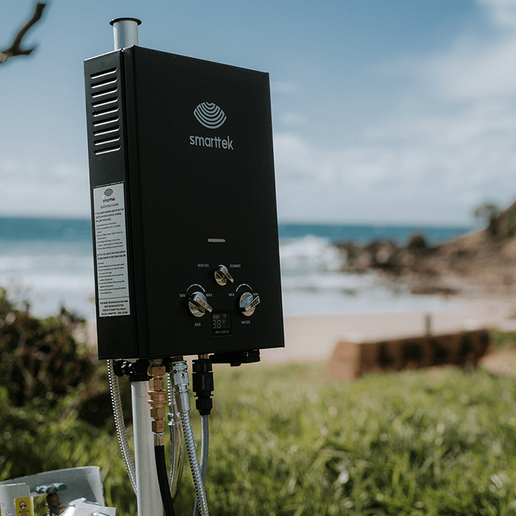 Smarttek Black 4.3LPM portable hot water system shown from the side in an outdoor setting.