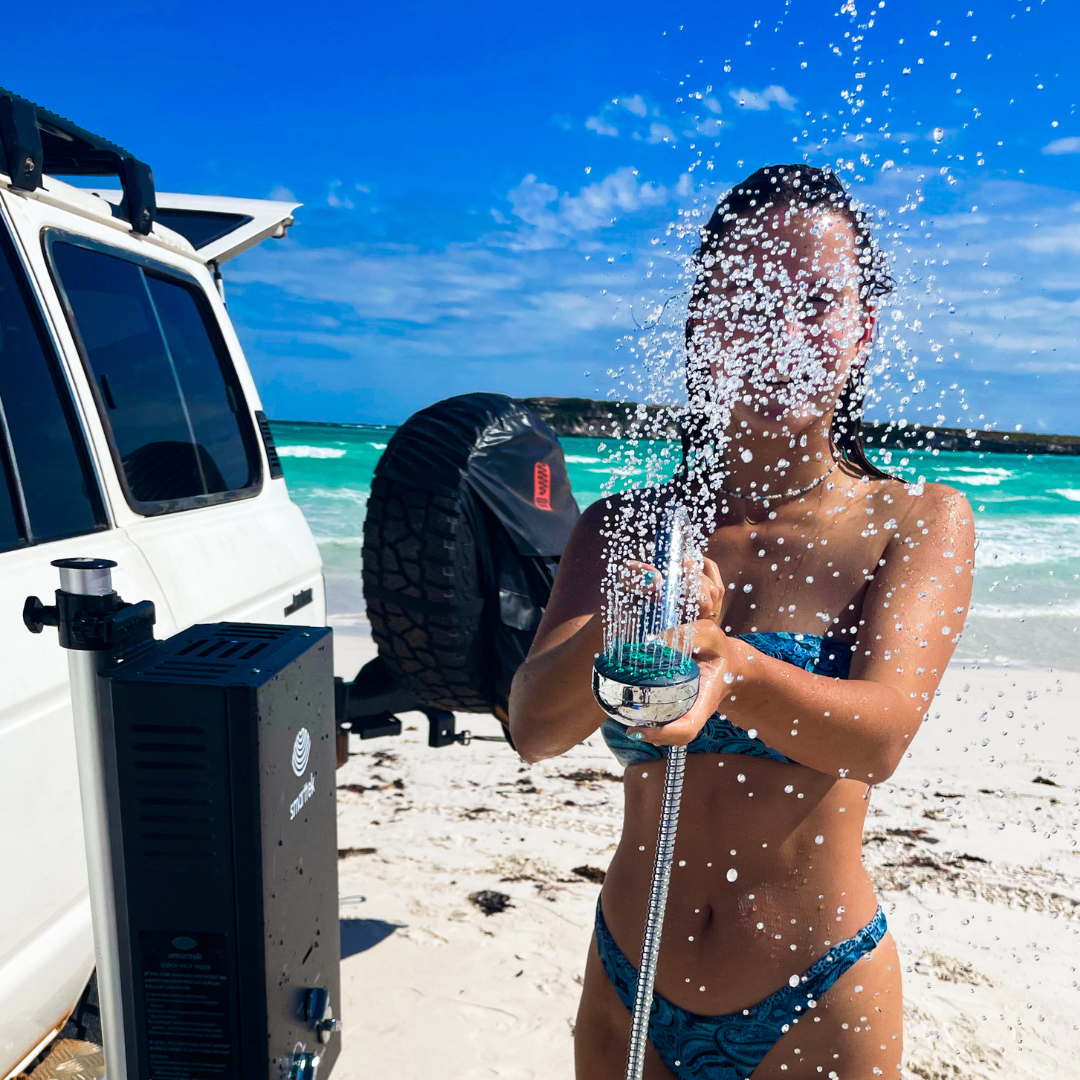 Person using a Smarttek Black 6LPM portable hot water system with handheld shower outdoors.