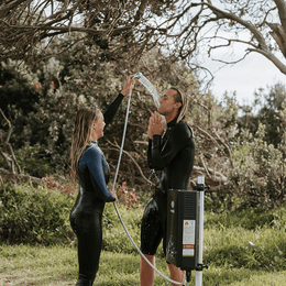 Two people using a Smarttek Black hot water unit with a handheld shower outdoors.