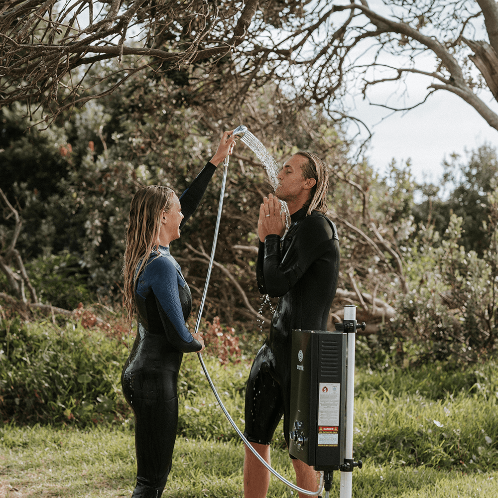 Two people using a Smarttek portable hot water system with a premium twist shower rose in an outdoor setting.