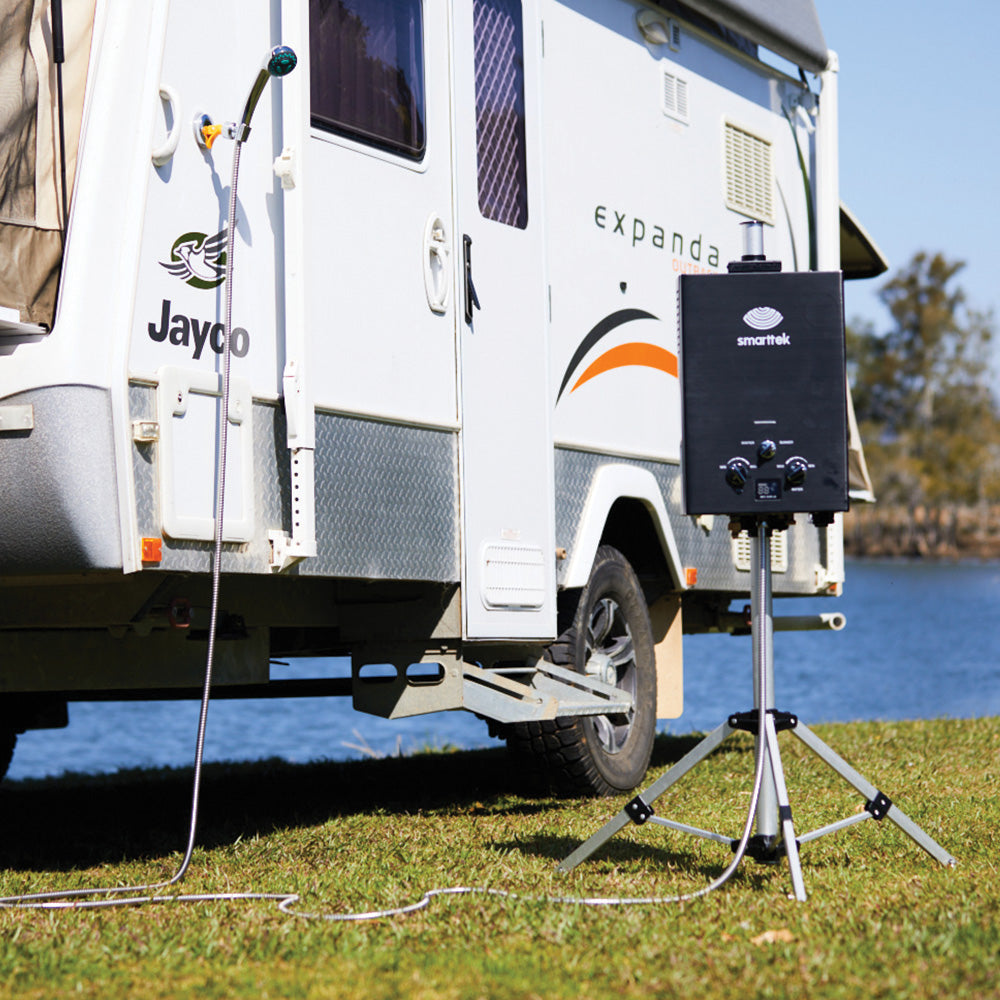 Smarttek hot water system connected to a caravan with a 5 metre shower hose in an outdoor campsite setting.
